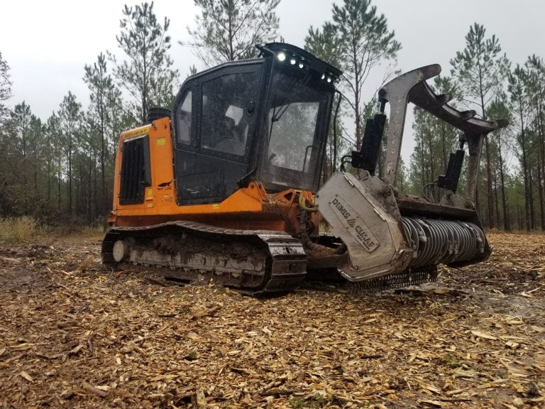 Orange tracked forestry mulcher with a Denis Cimaf drum mulcher attachment, surrounded by wood chips in a cleared pine forest area